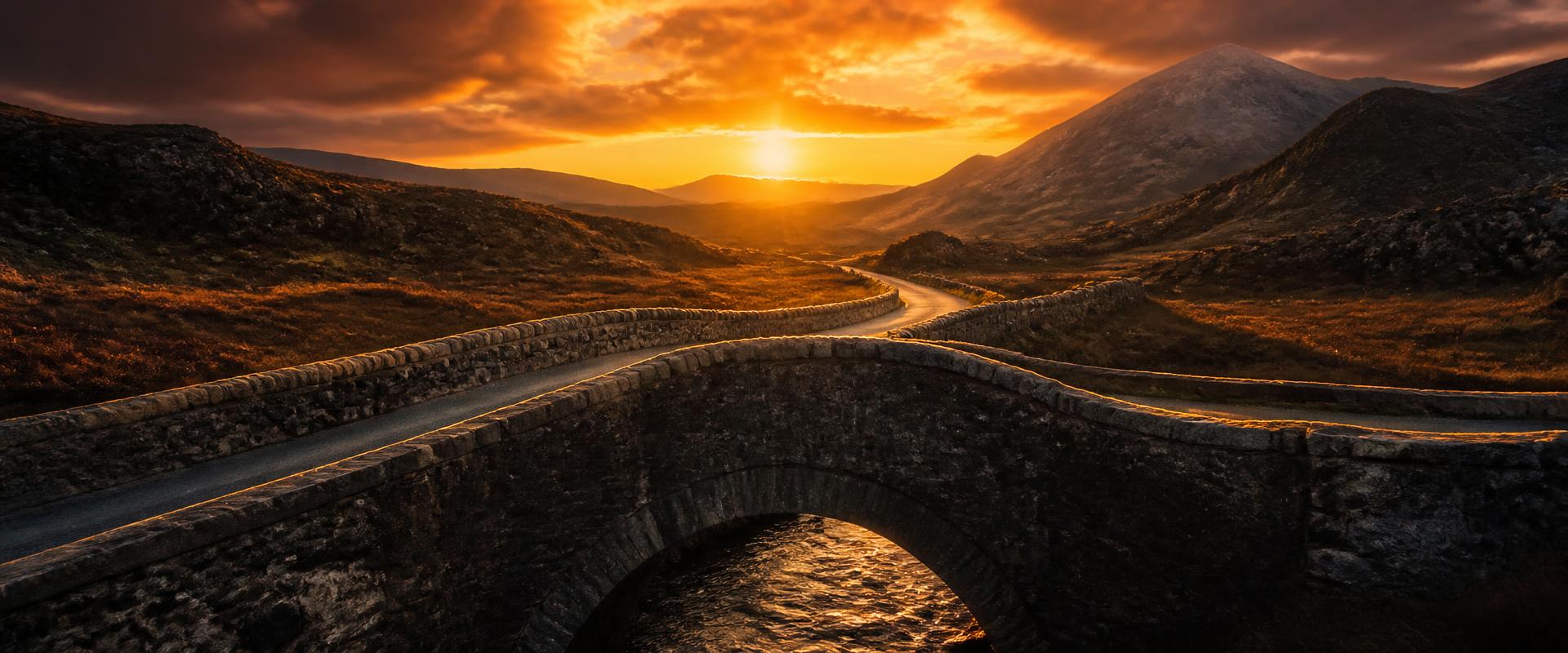 Stone bridge glowing at sunset, leading toward a winding road